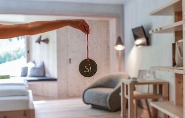 Hand hält ein rundes Schild mit der Aufschrift „Sì" in einem Designzimmer des Hotel Bühelwirt, Ahrntal